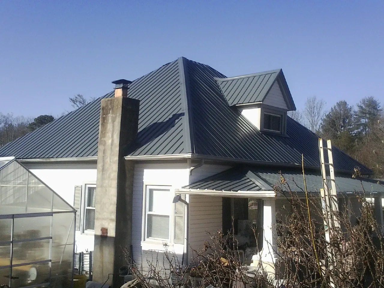 Dark blue standing seam metal roof on a white farmhouse with dormer — Slate & Tile Roof Repair by Roofing Brothers in Buckeystown