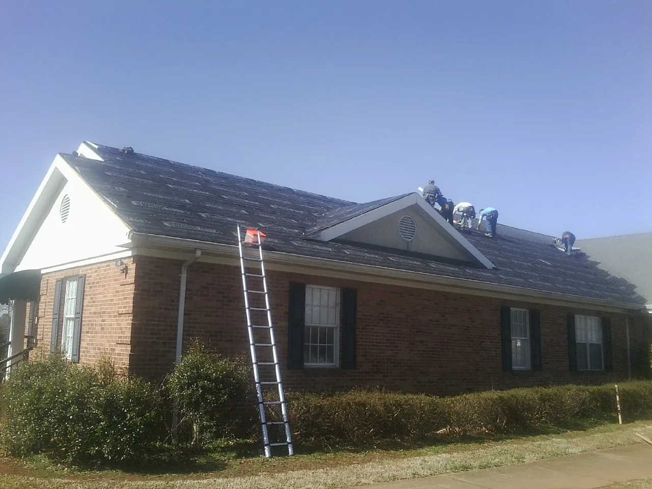 Crew tearing shingles off a brick ranch roof with a ladder set — Metal Roof Repair work by our crew in Buckeystown