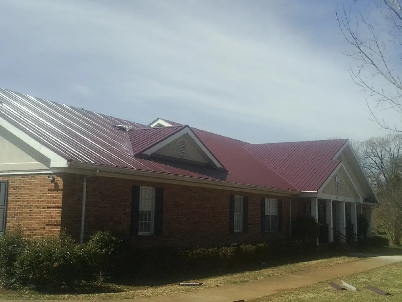 Red metal roof with gabled entries on a long brick building, from a Hail Damage Roof Repair job in Buckeystown