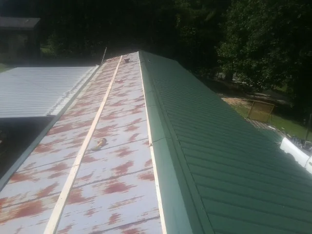 Old rusted panels beside newly installed green metal roofing — Wind Damage Roof Repair by Roofing Brothers in Buckeystown