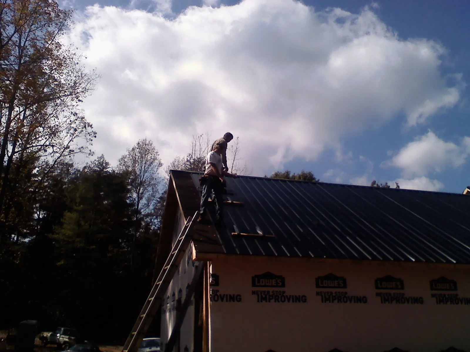 Roofer fastening dark metal panels high against a cloudy sky, from a Roof Inspection job in Buckeystown