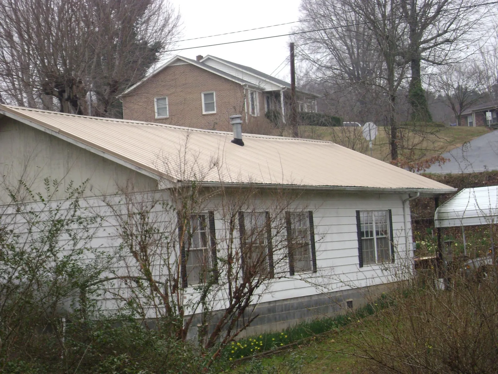 Tan metal roof on a white sided house set into a hillside — Commercial Roofing by Roofing Brothers in Buckeystown